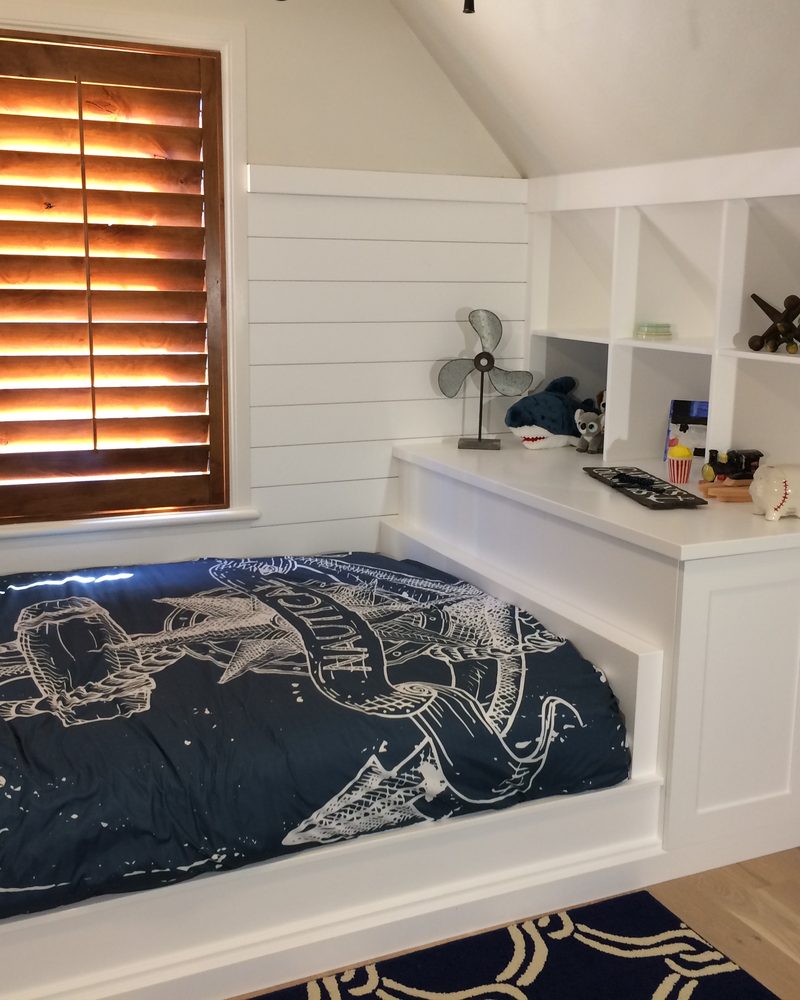 White built-in drawers, shelving, and daybed around a window